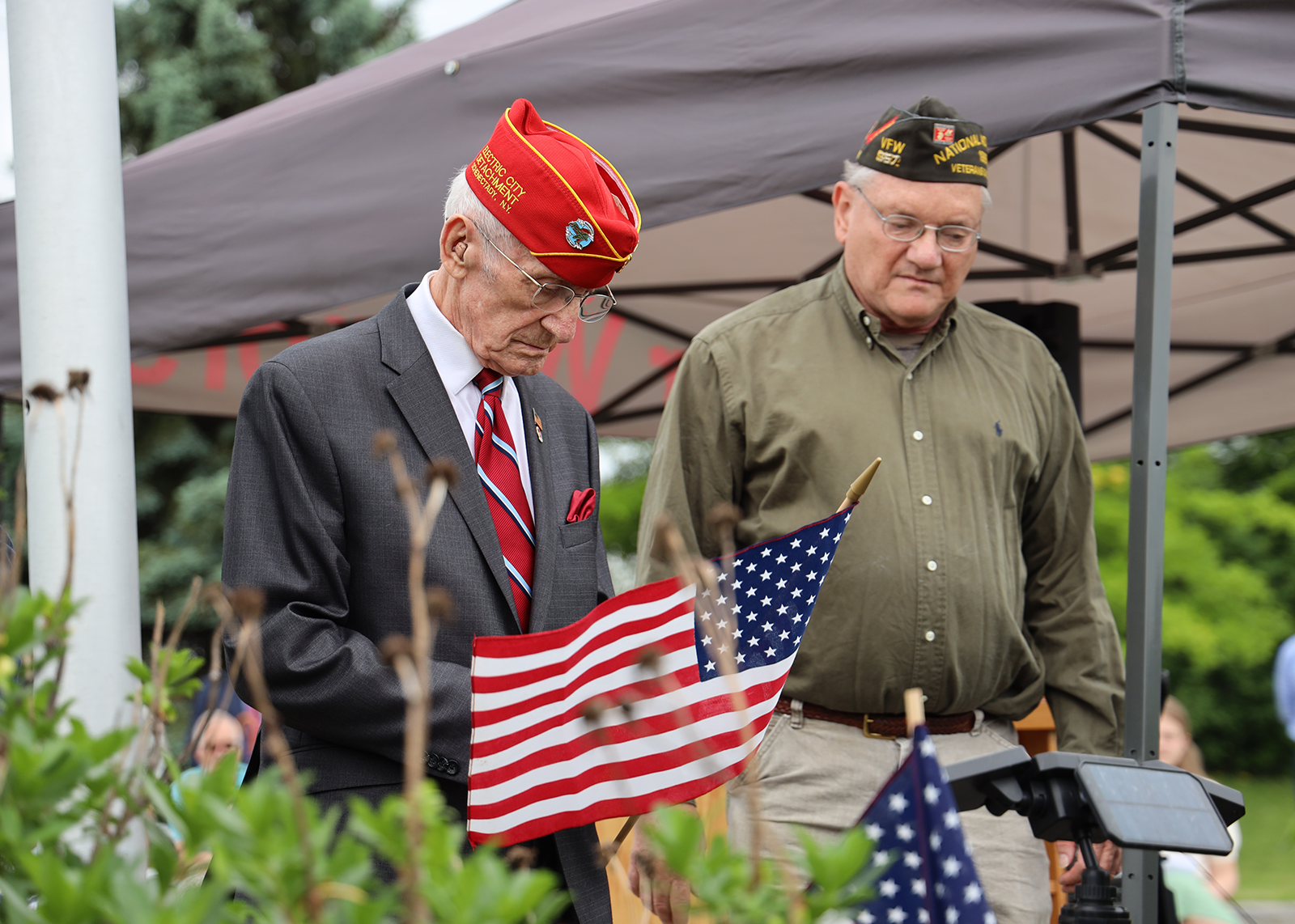 Two veterans wearing military hats gaze solemnly at the ground