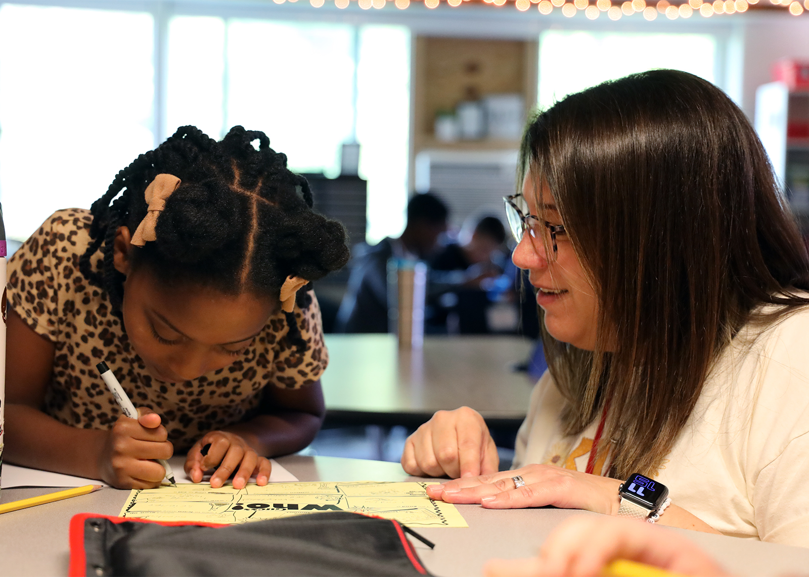 teacher kneeling down to help student working on a worksheet