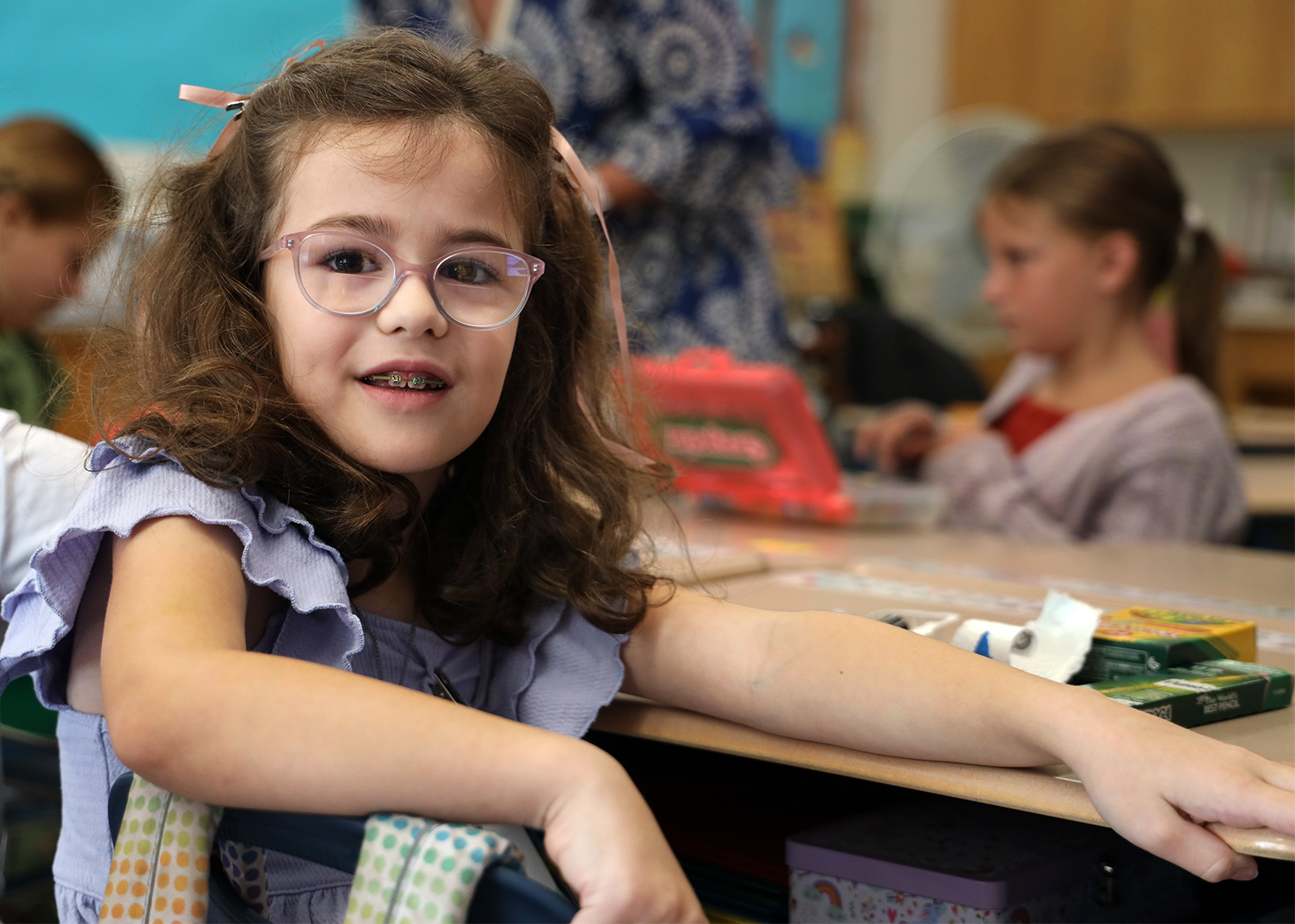 student with glasses smiles at desk