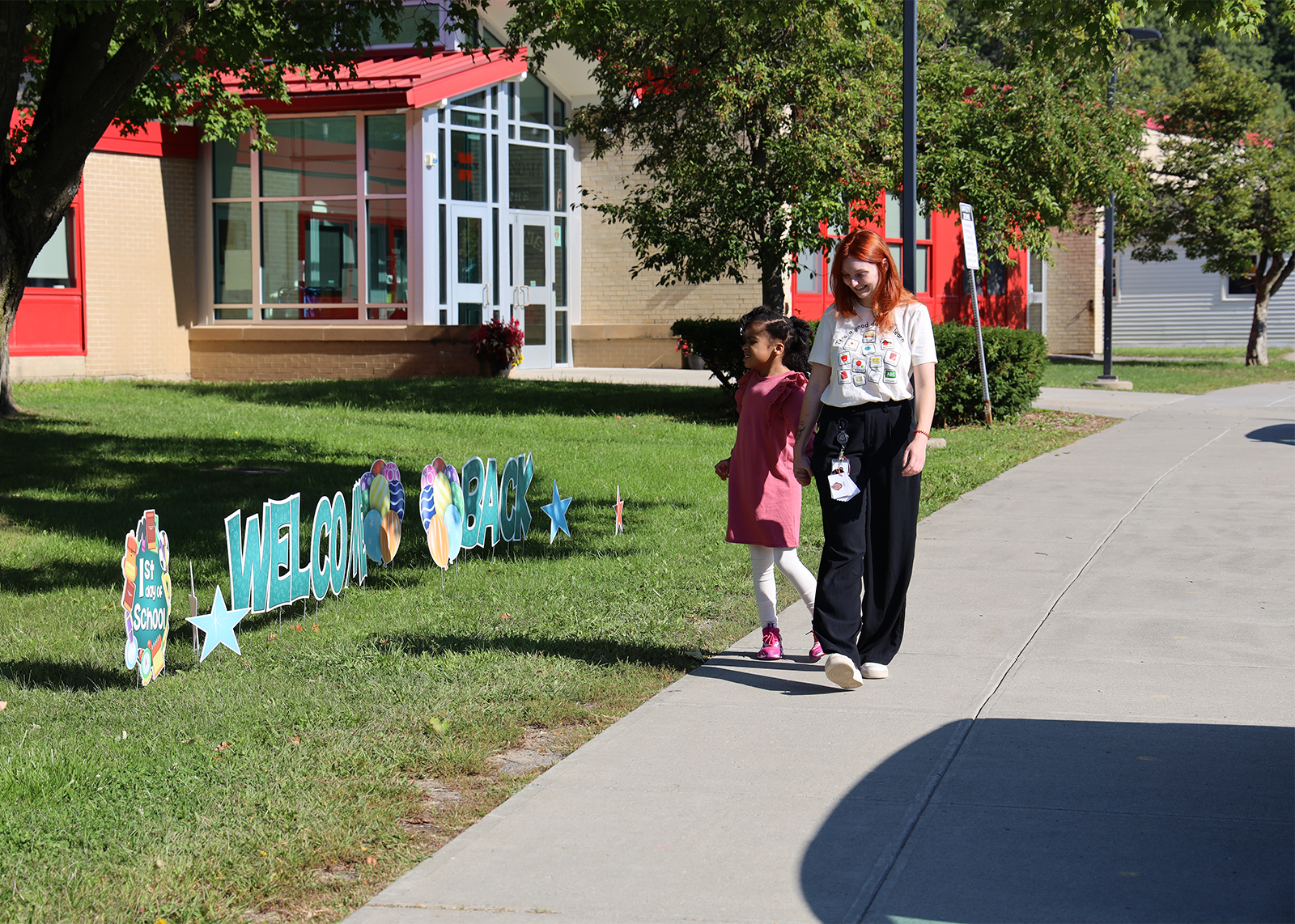 student walking with teacher outside school with sing that says welcome back