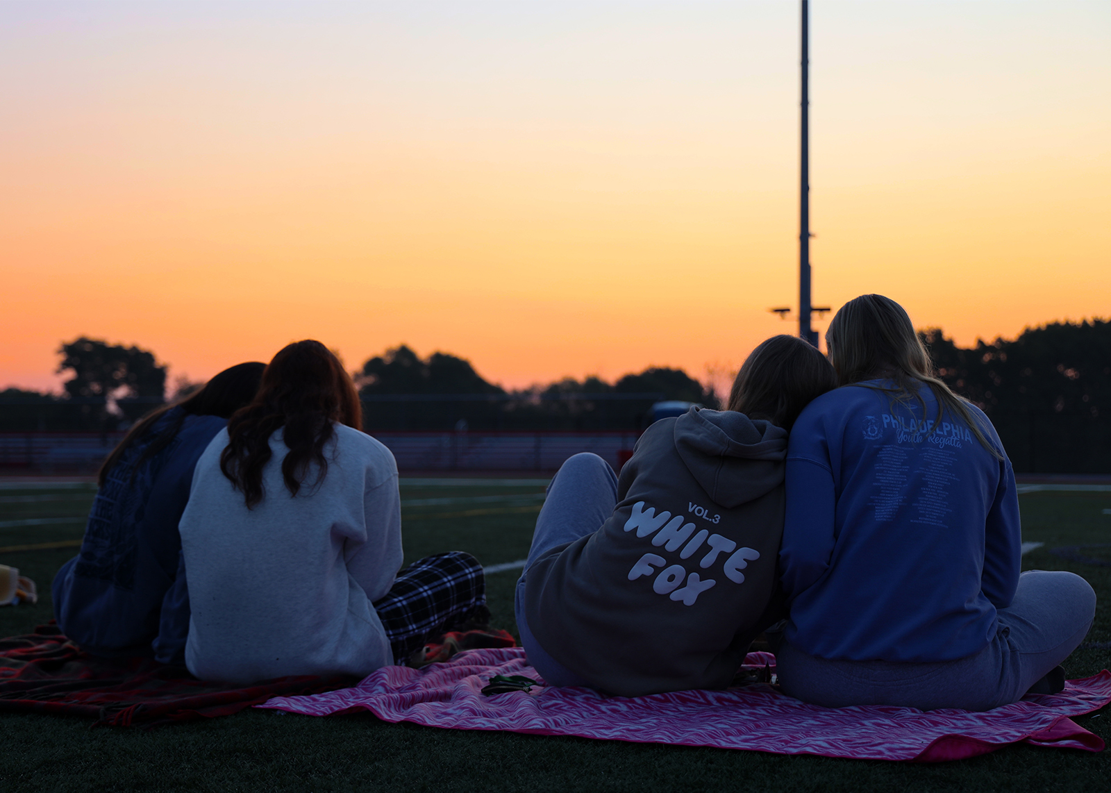 friends on blanket face sunrise on football field