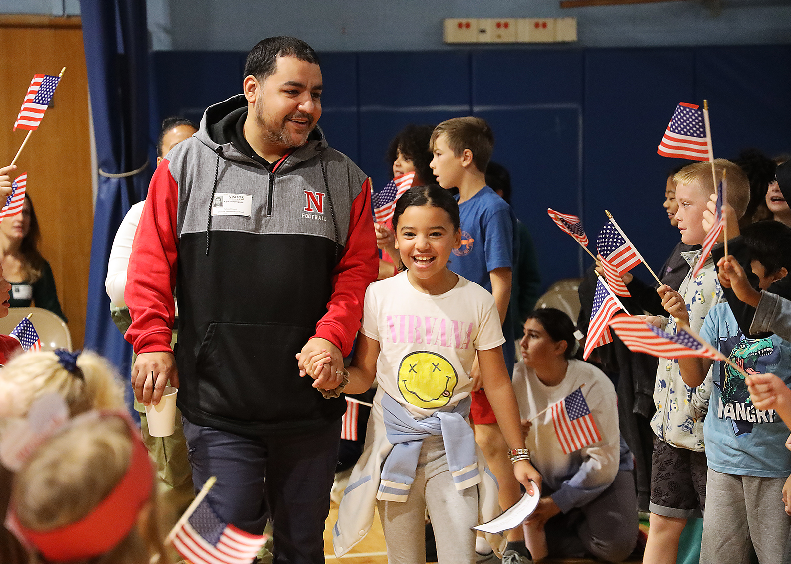 student and veteran smiling falnked by elemetary kids with falgs