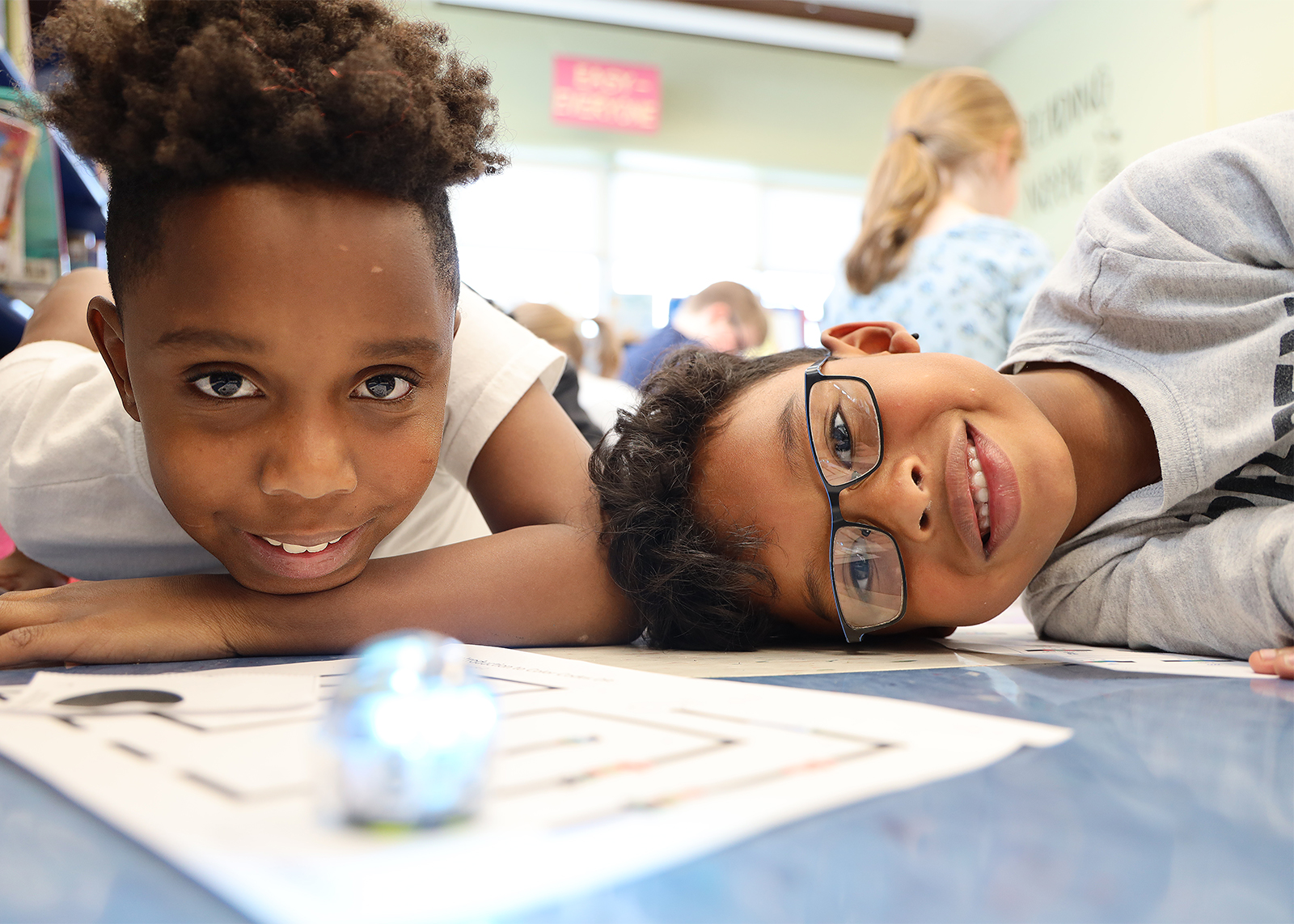 fourth and first grader smile with Ozobots in forground