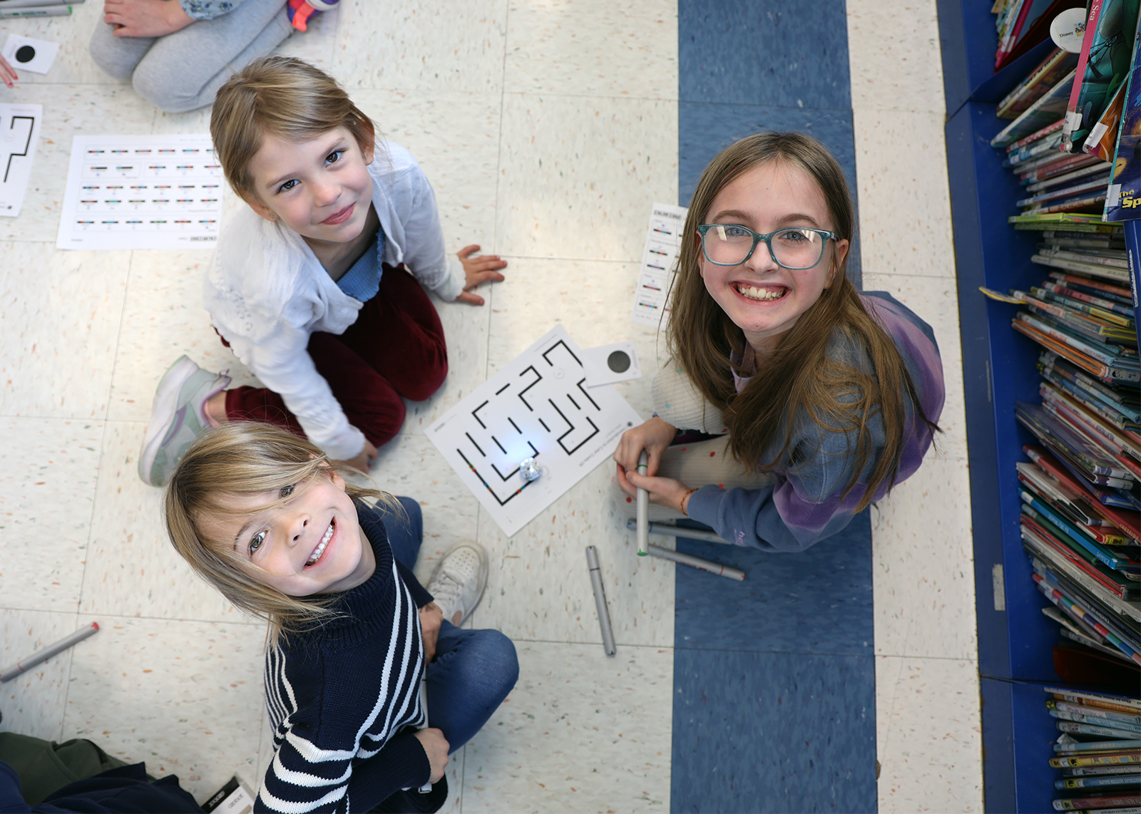 three elementary students look up for photo in library