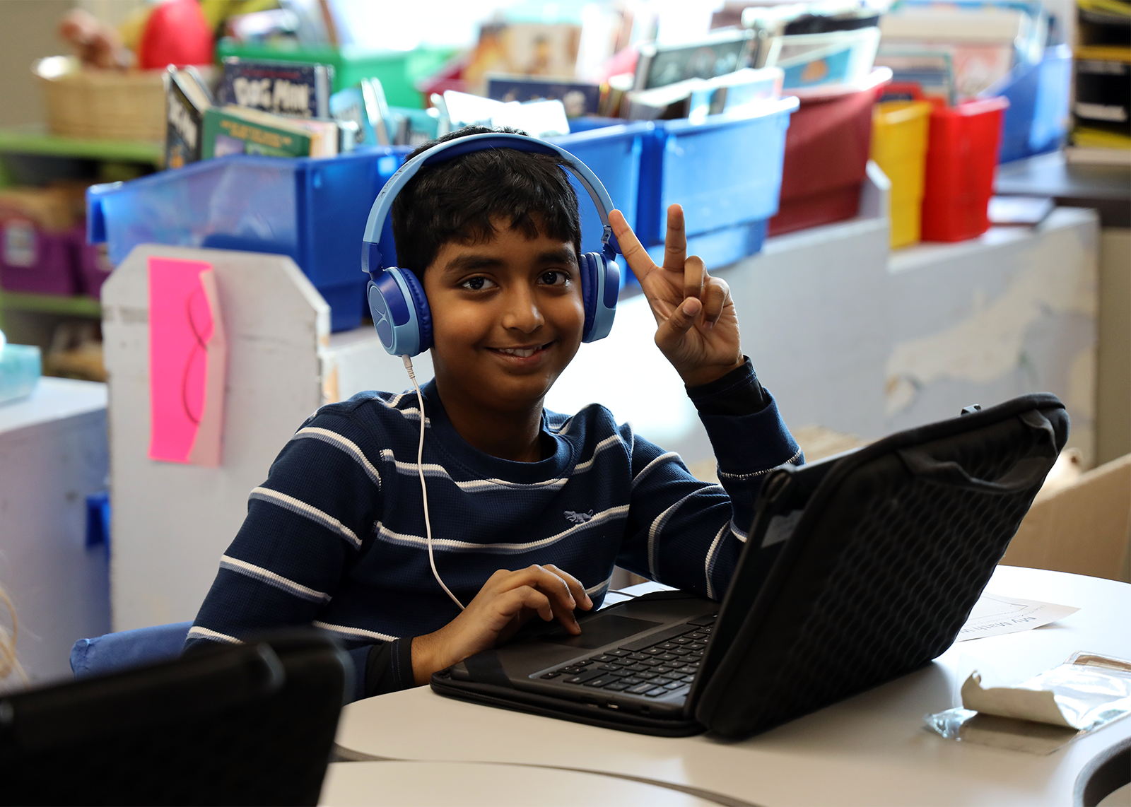 student on chromebook giving peace sign