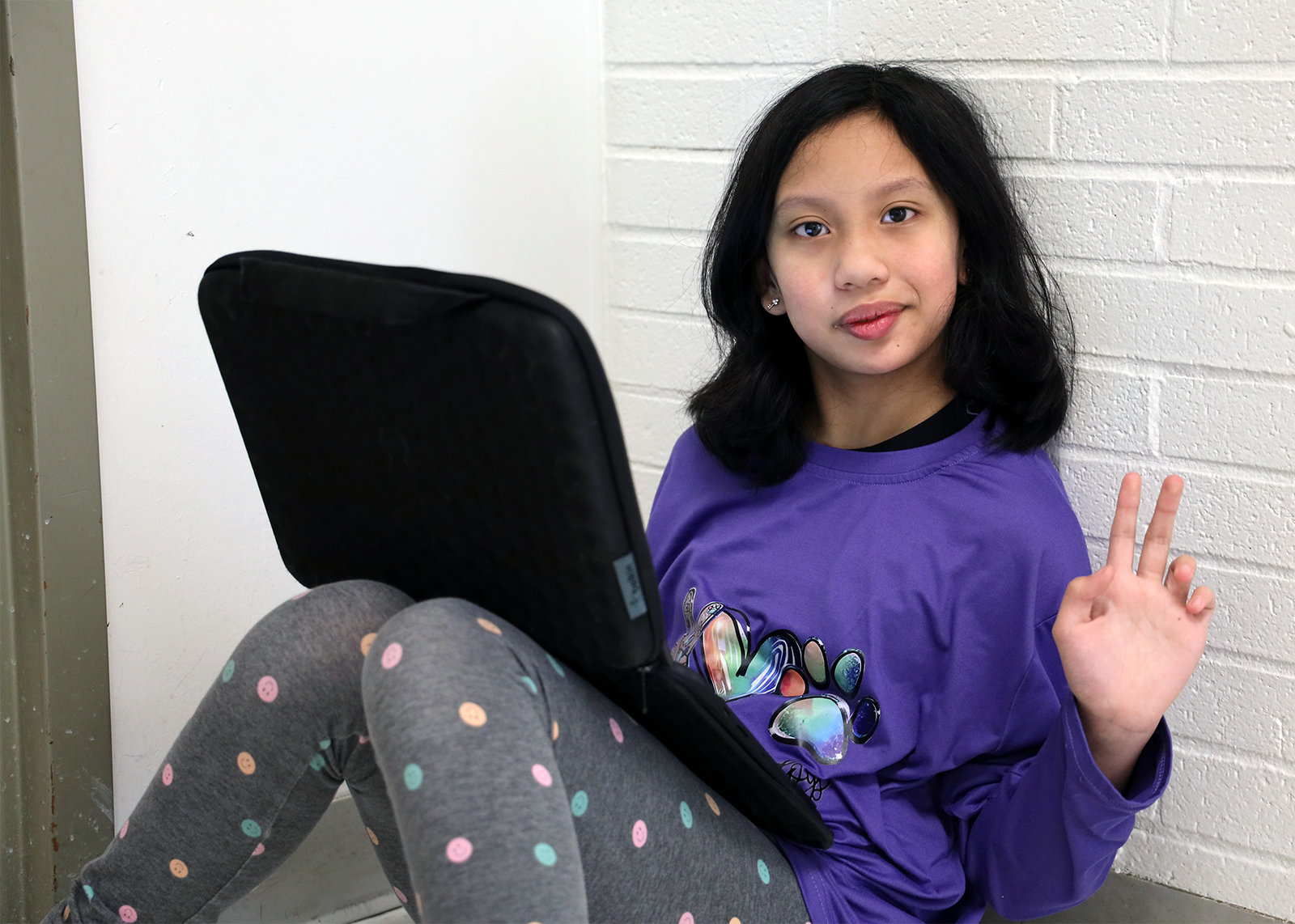 student in hallway on chromebook giving peace sign