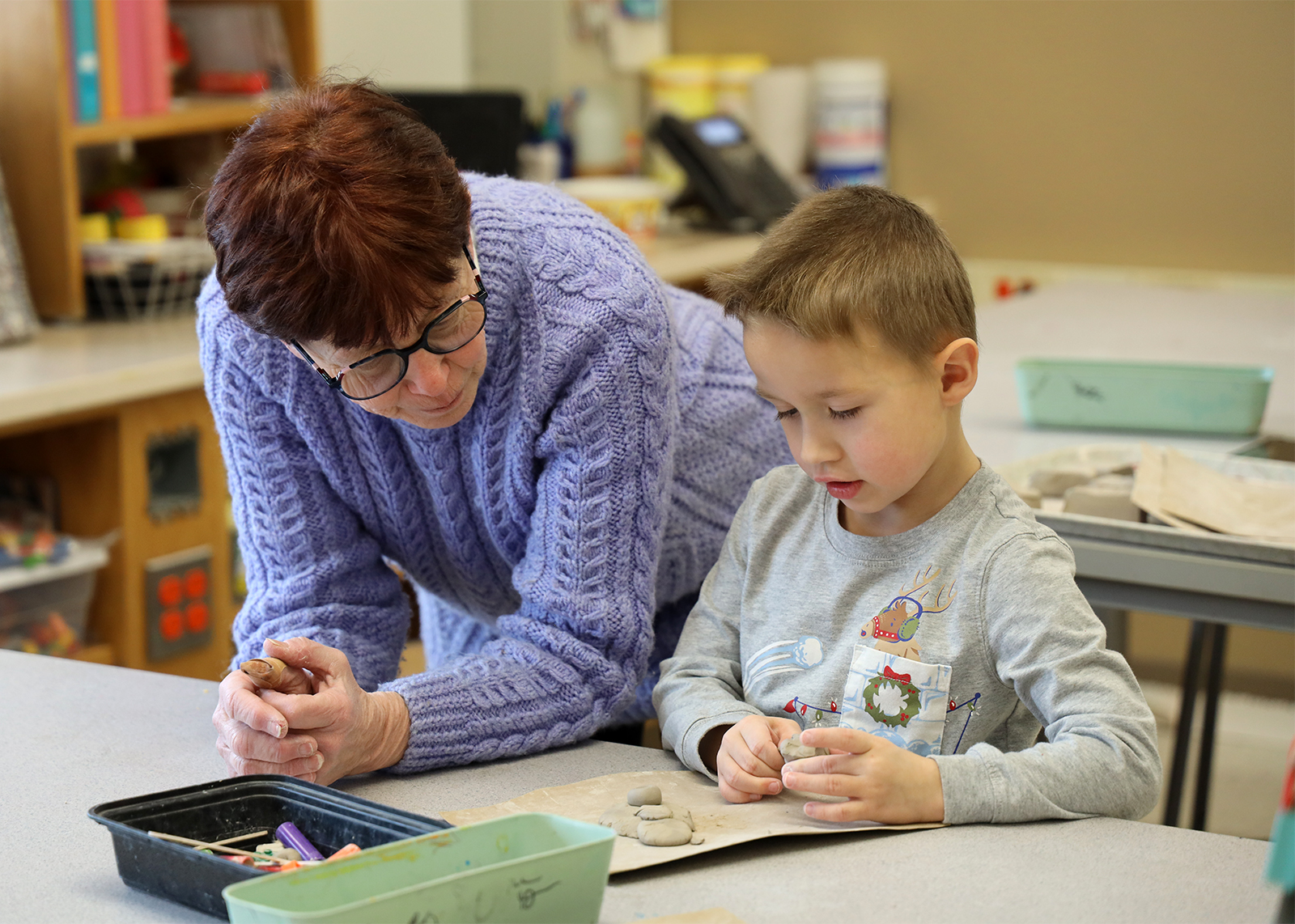 teaching assistant helps Kindergartner with clay