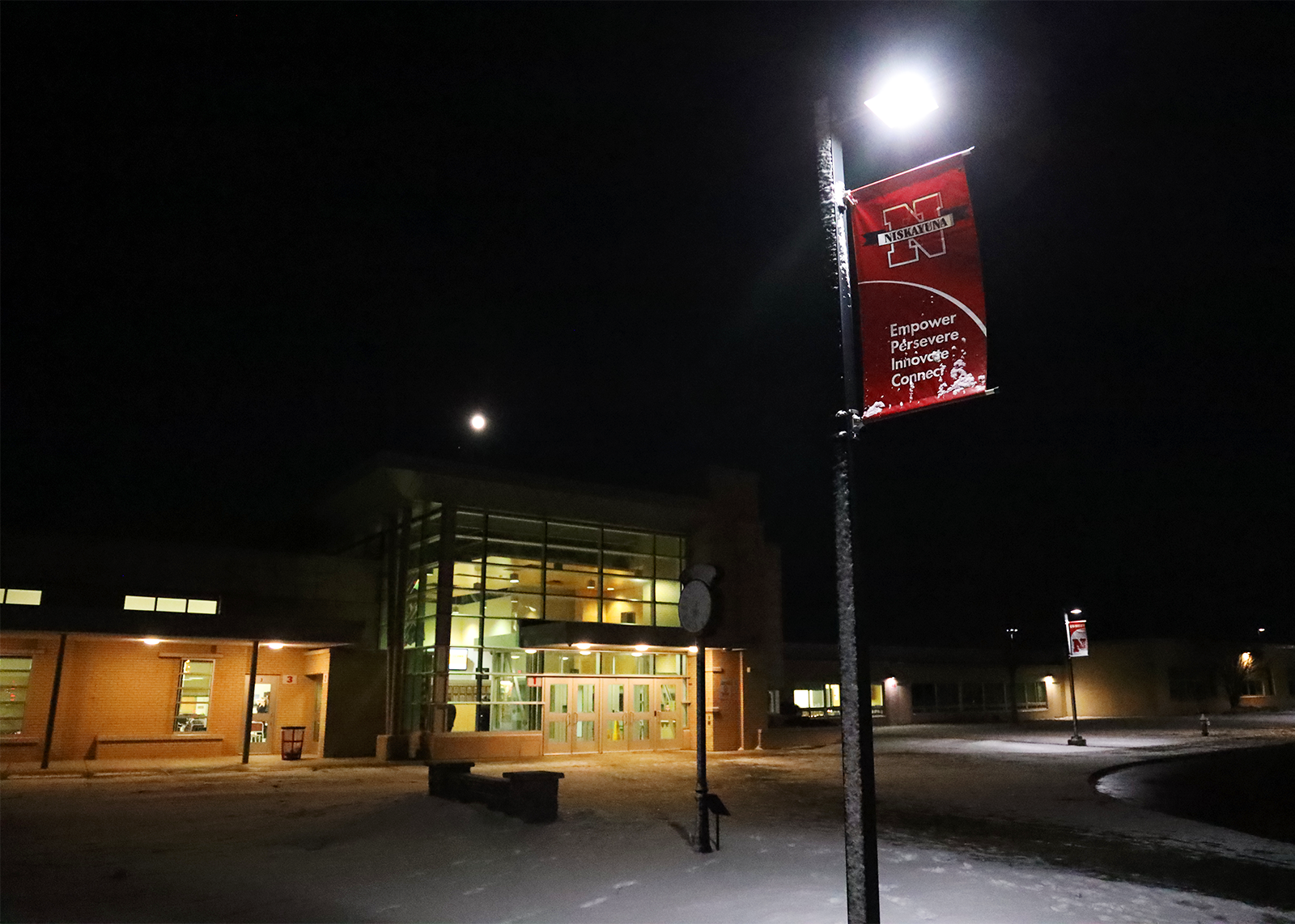 flag poke with snow and school building lit up at night