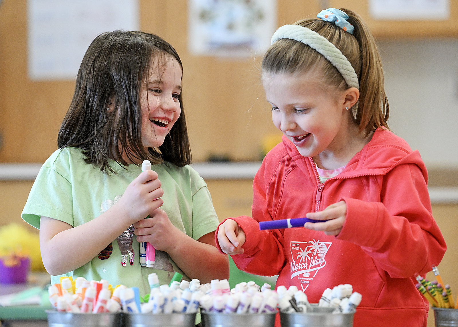 two kindergarten students smile over markers